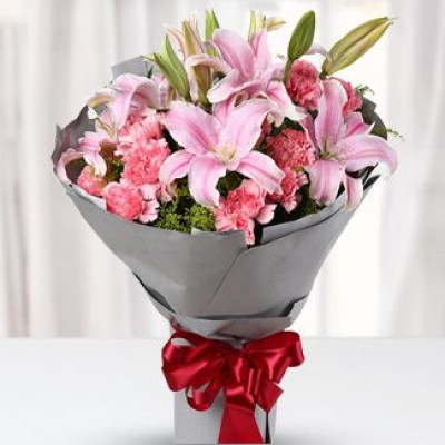 Bunch of Pink Carnation 12 stems & 2 stems of pink perfume lilies in round style paper wrapped, red gift ribbon tied mixed bouquet. Always There
